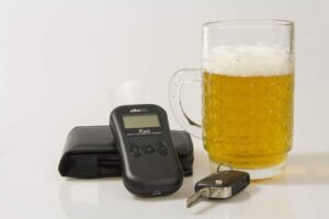 A glass of low alcohol beer beside a set of car keys and a breathalyzer test
