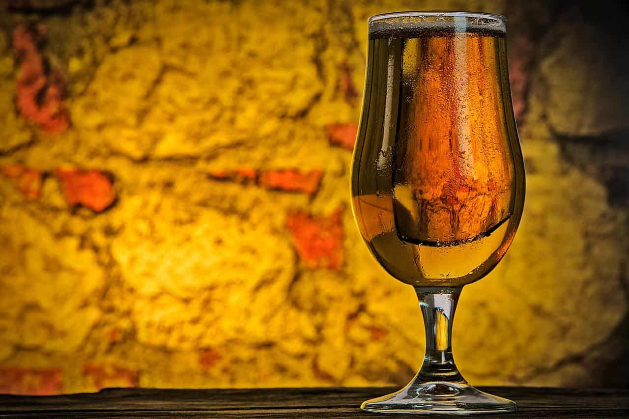 Glass of alcohol free beer in front of a brick wall with a yellow hue